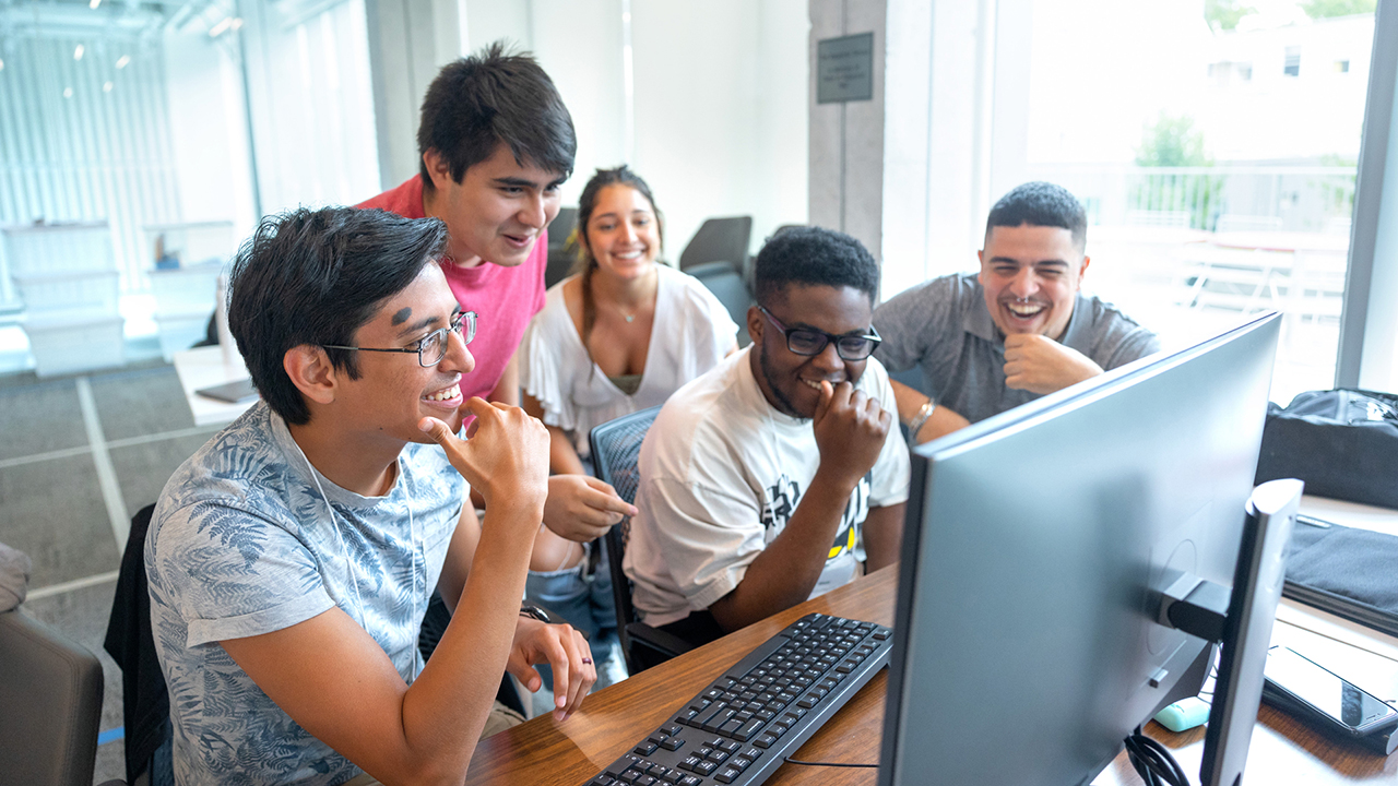 Several students laughing with eachother while looking at a computer screen.